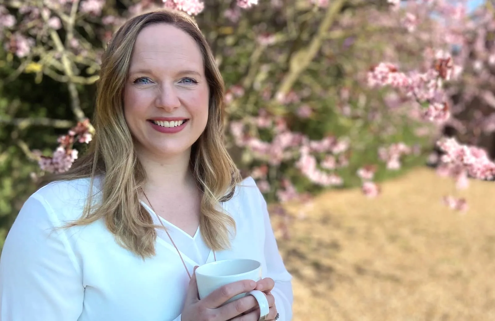 Helen Bennett holding a cup beneath blossom trees